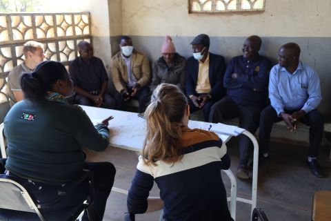 Männergruppe in Chikombedzi, Simbabwe, sitzt im Halbkreis und diskutiert mit zwei Frauen über Gesundheit und Diabetes.